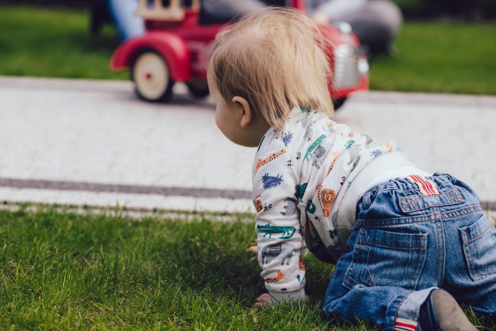 A toddler crawling on green grass outdoors near a toy car, enjoying a sunny day.